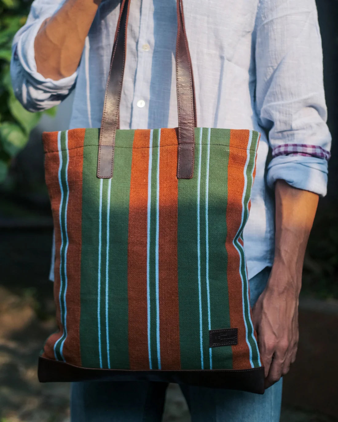 Person holding a striped tote bag with a blurred natural background