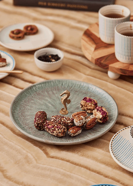 Assorted snacks on a plate with a decorative seahorse figurine on a wooden table.