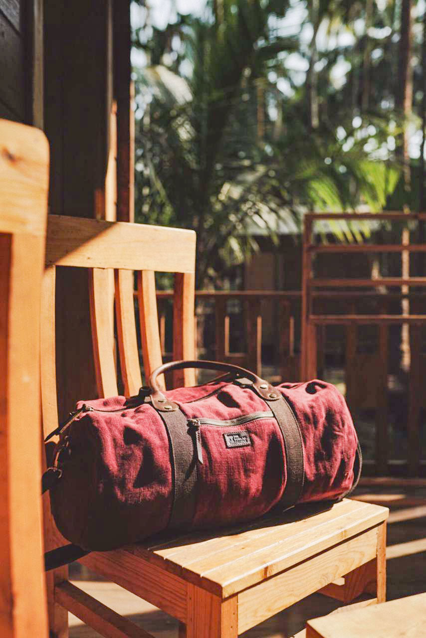 Red duffel bag on a wooden chair with a blurred outdoor background