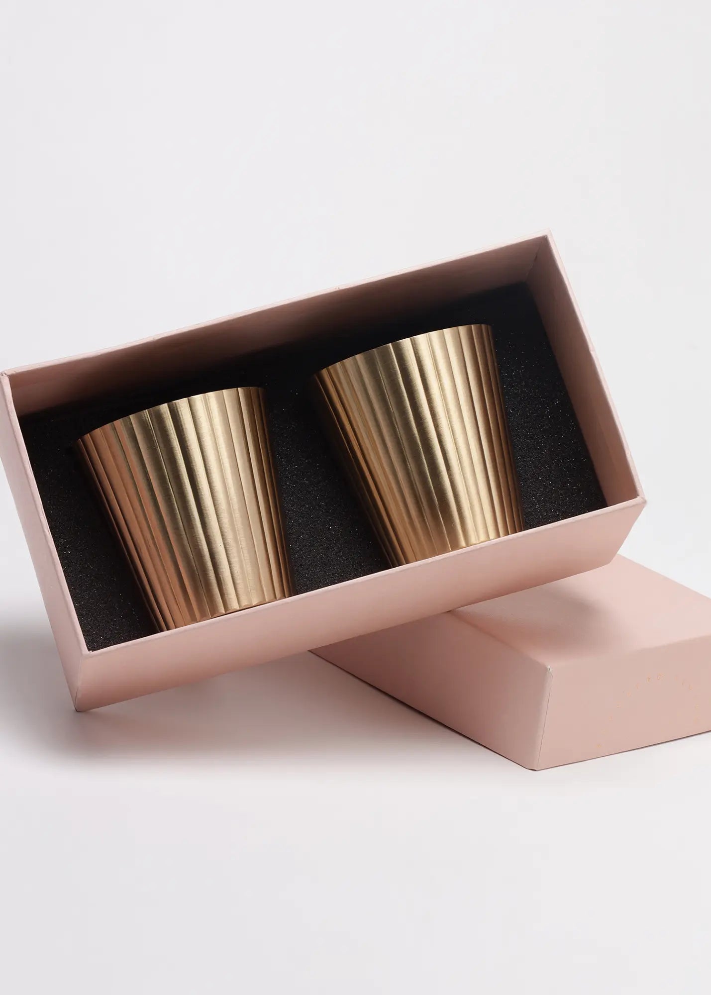 Two gold tumblers in an open pink box on a light background