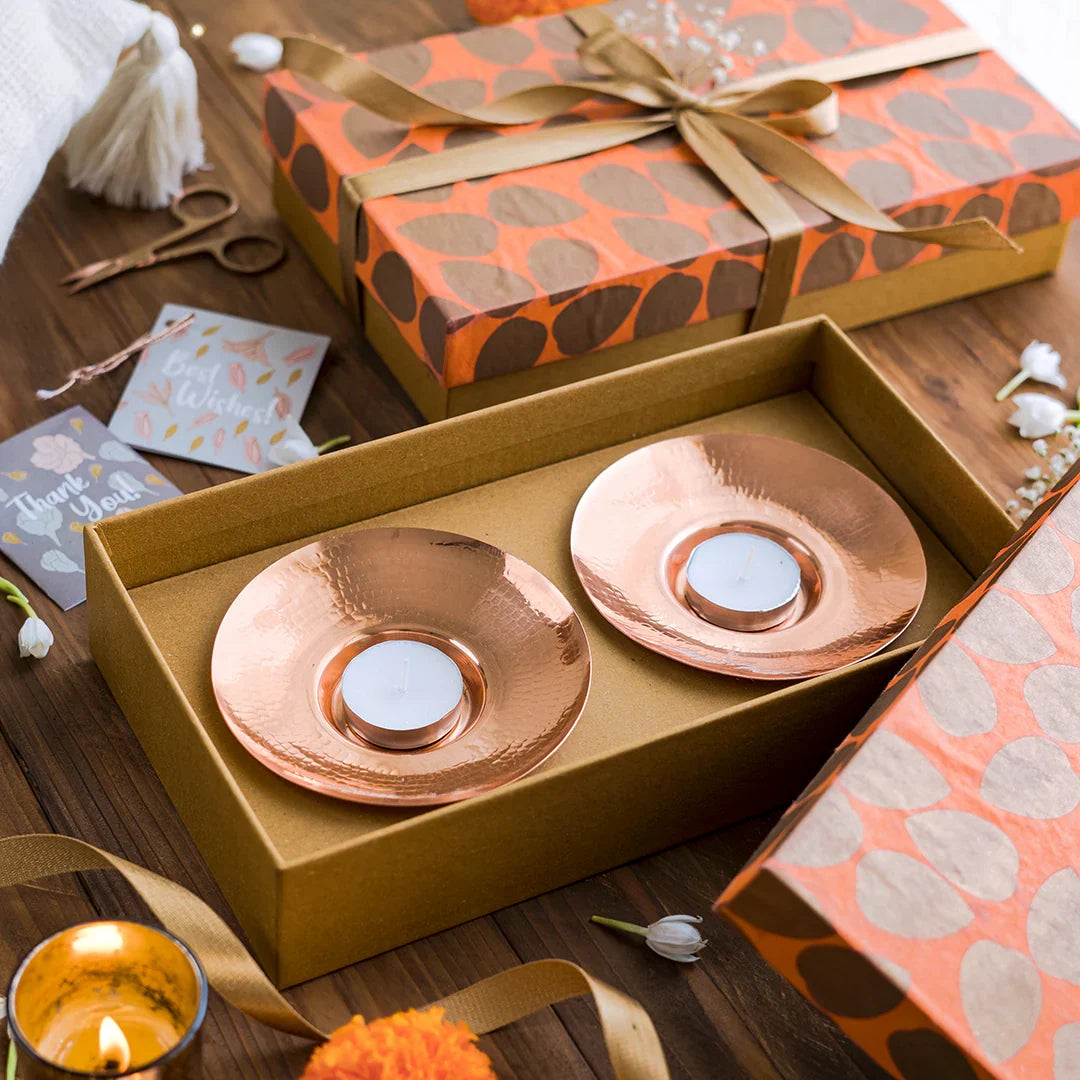 Copper candle holders in a box with decorative packaging on a wooden surface.