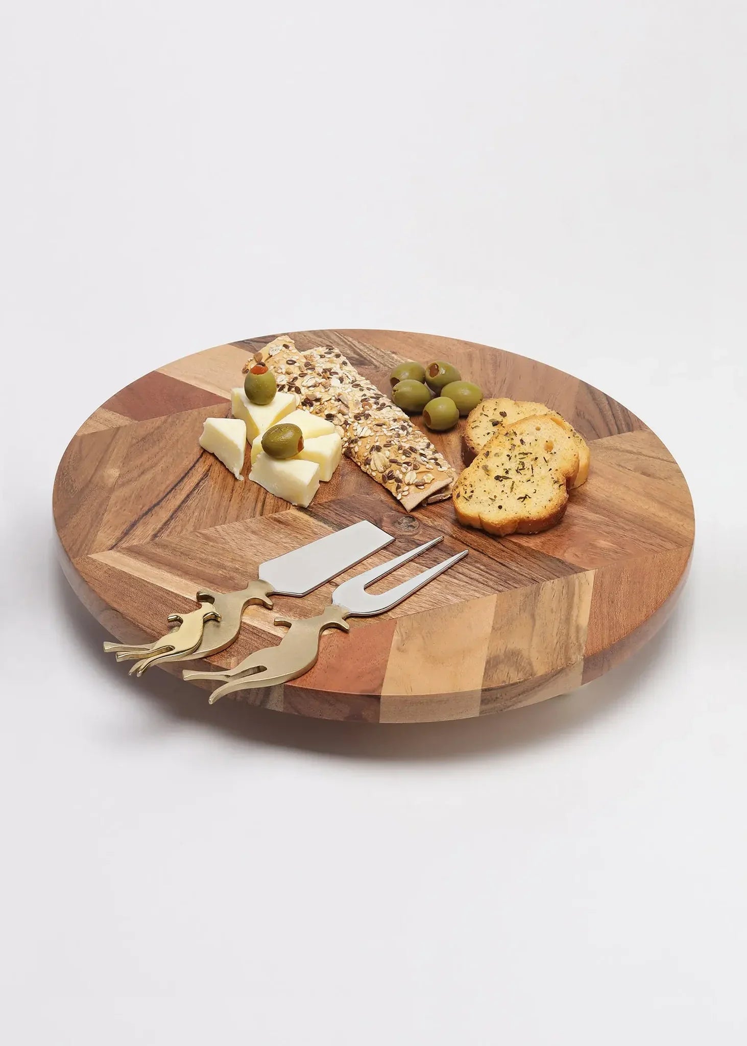 Wooden cheese board with cheese, crackers, and utensils on a white background