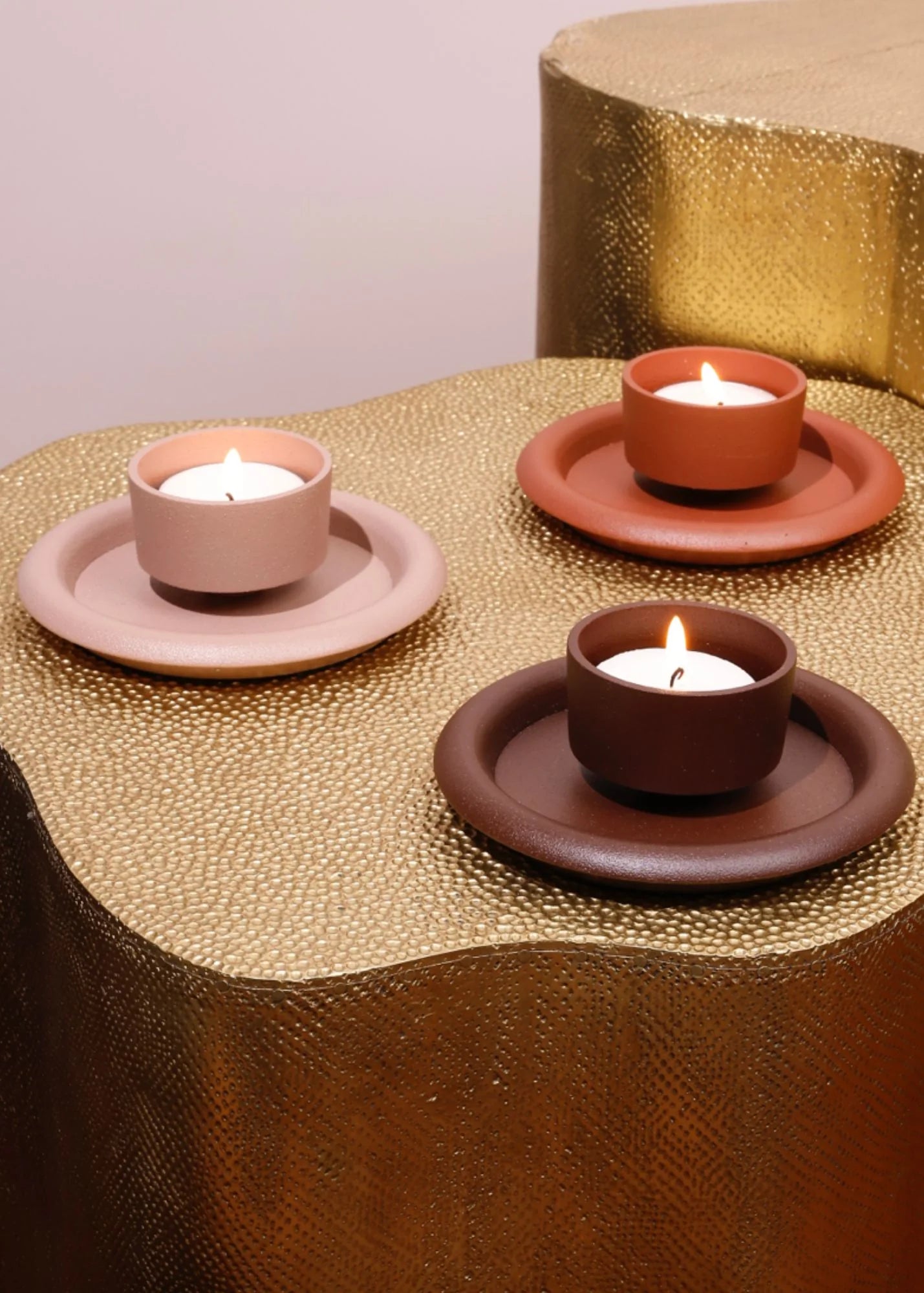 Three terracotta candle holders with lit candles on a textured gold surface.
