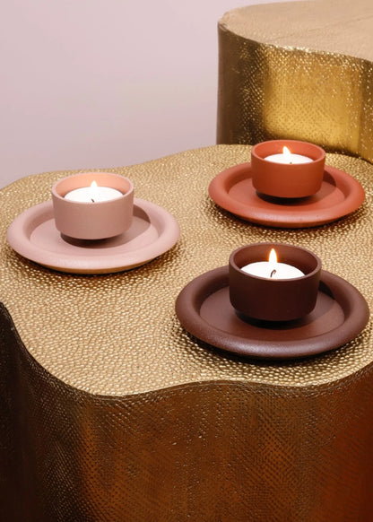 Three terracotta candle holders with lit candles on a textured gold surface.