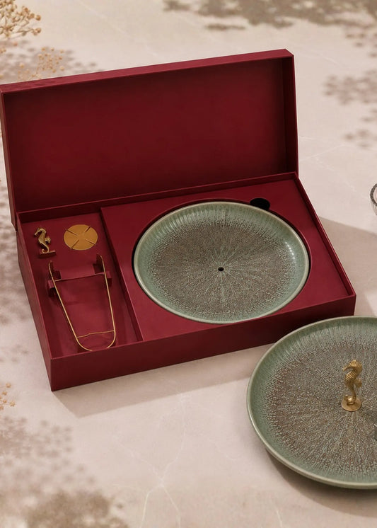 A ceramic tea set with a textured light green glaze and gold-toned handles, presented in an open dark red gift box alongside a matching lid on a beige patterned surface.