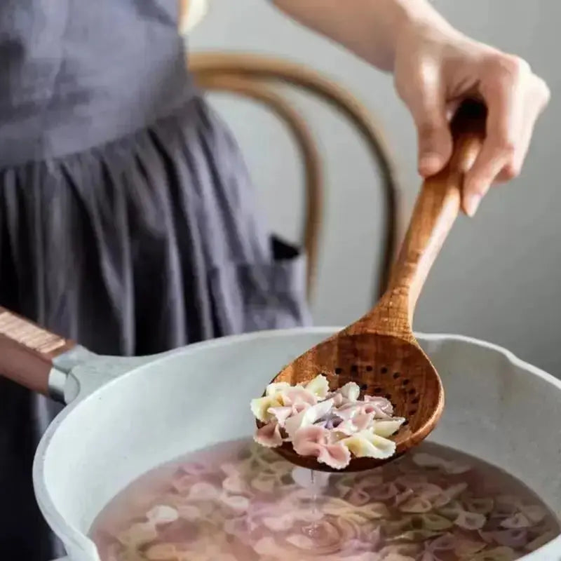 Person holding a wooden spoon with noodles over a pot of soup