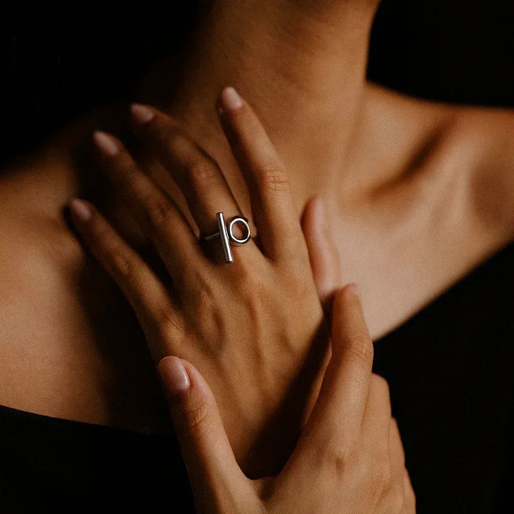 Close-up of a hand wearing a silver ring with a unique design, against a dark background.