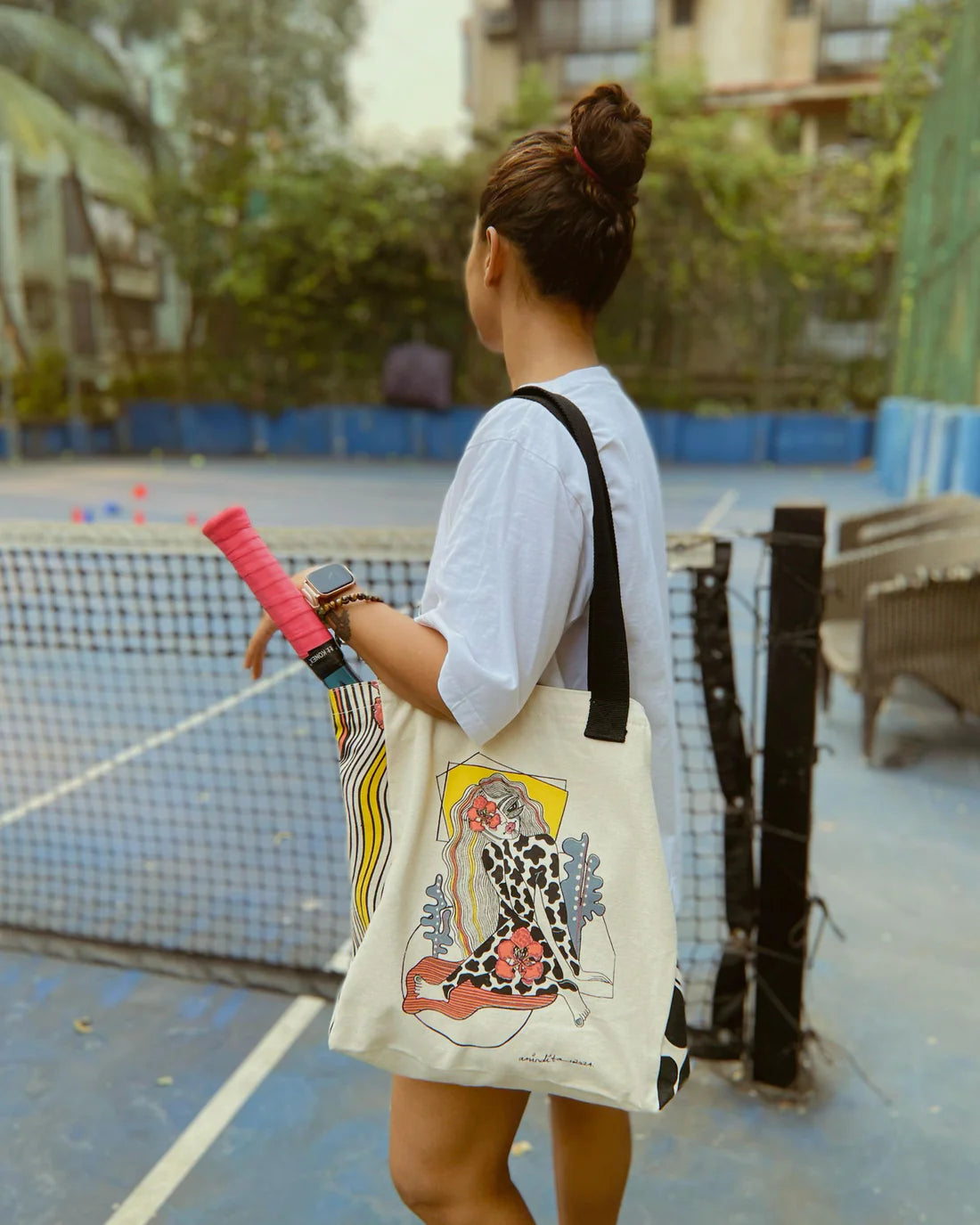 Person holding a tote bag with a design on a tennis court