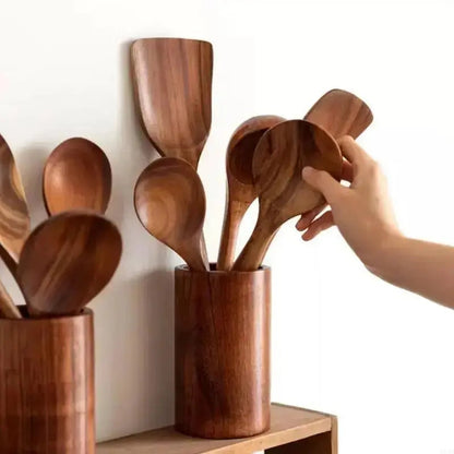 Wooden spoons in a wooden holder with a hand reaching in to grab one, on a light background.