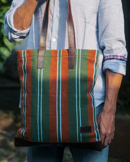 Person holding a striped tote bag with a blurred natural background