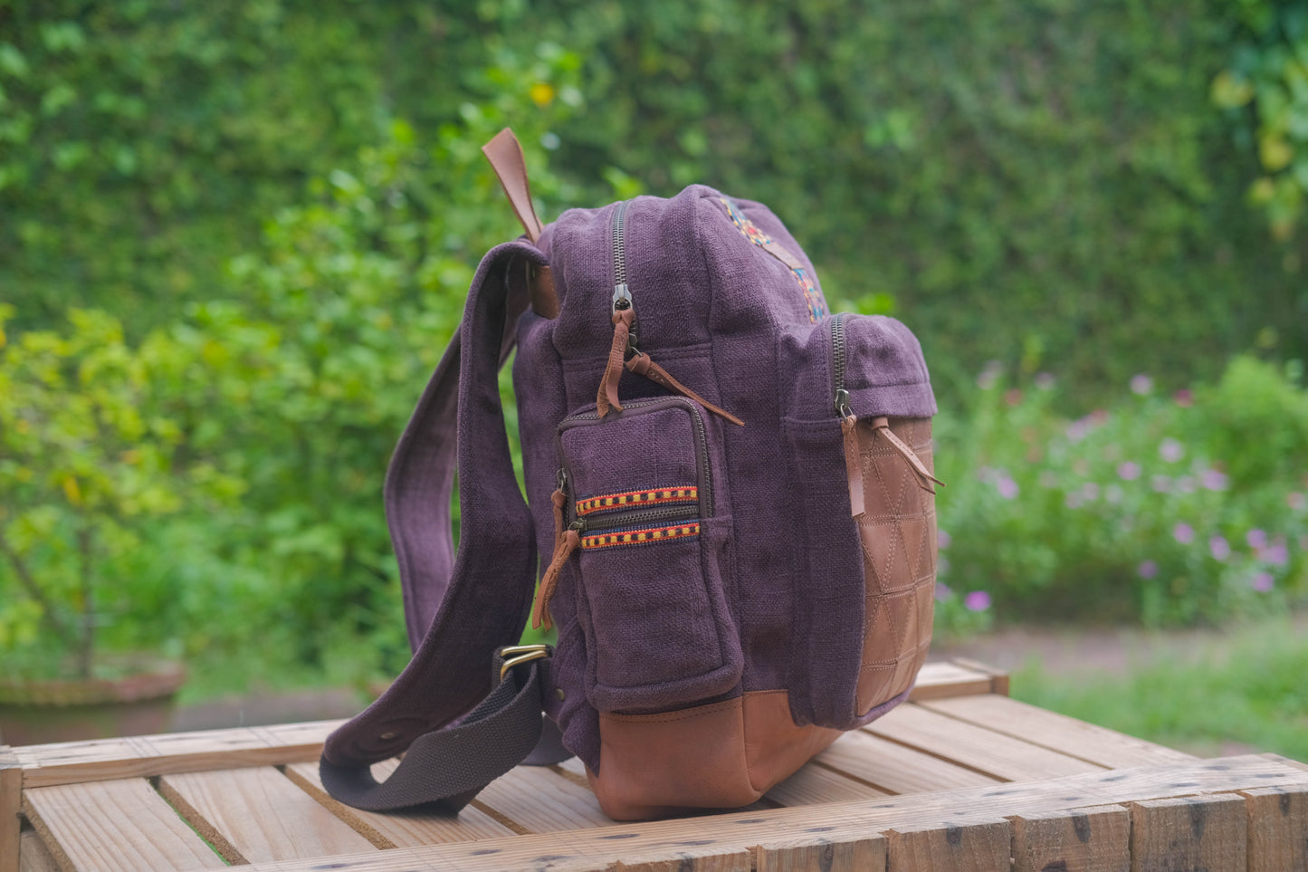 Purple and brown backpack on a wooden surface with a blurred green outdoor background