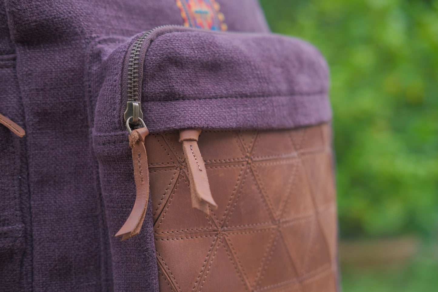 Close-up of a purple fabric with brown leather patch and zipper, blurred green background