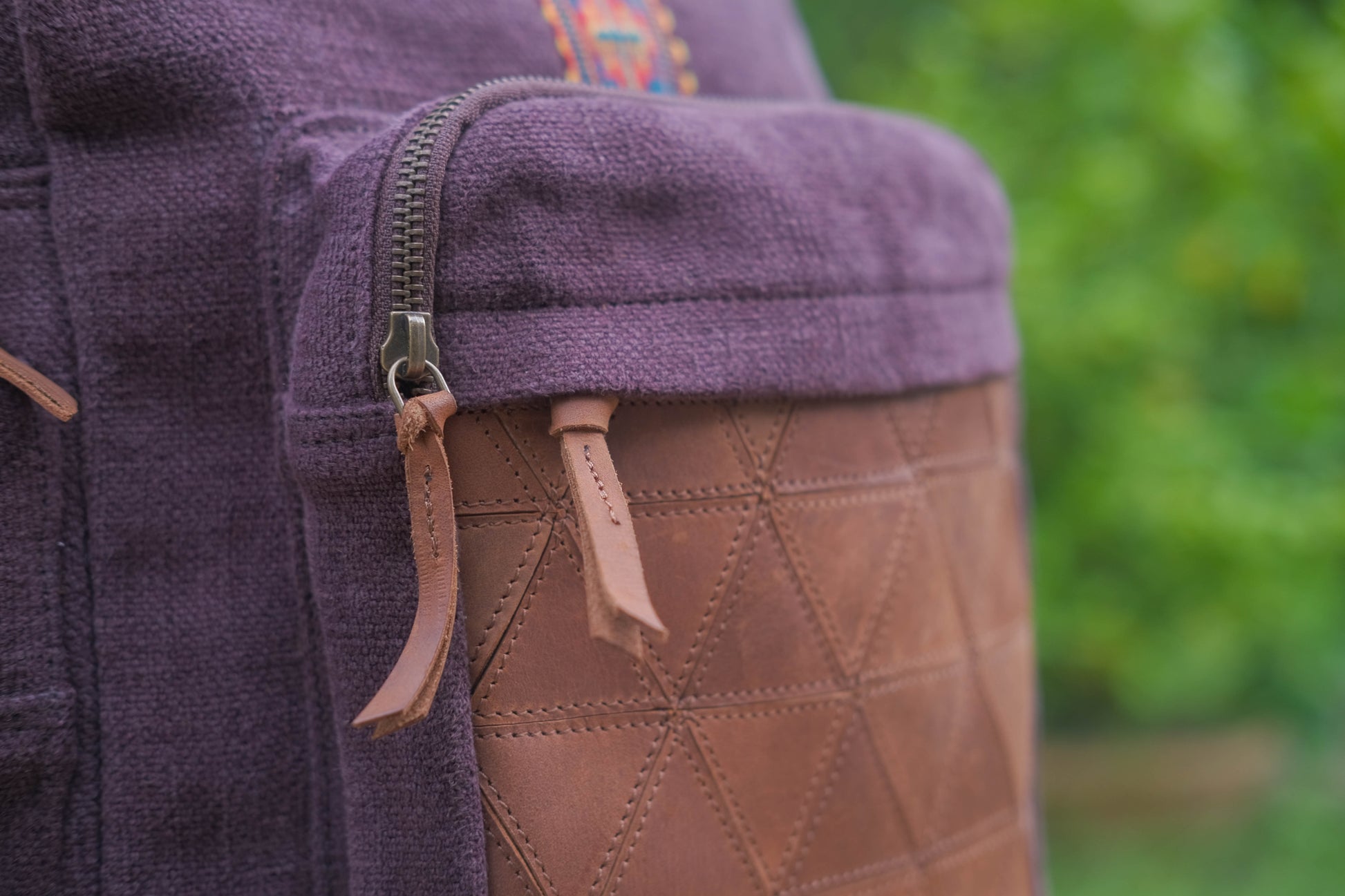 Close-up of a purple fabric with brown leather patch and zipper, blurred green background