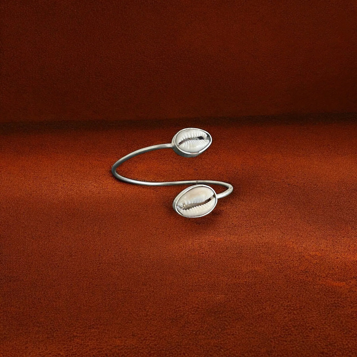 Silver open cuff bracelet with shell-like designs on a brown fabric background