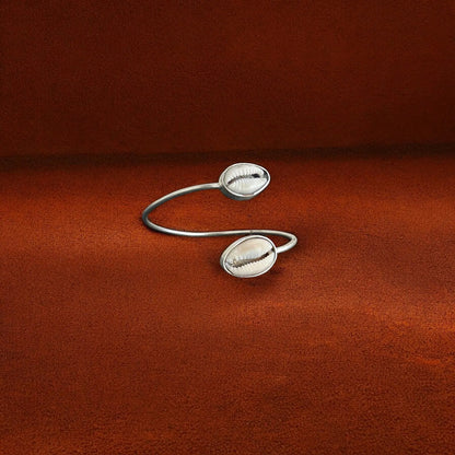Silver open cuff bracelet with shell-like designs on a brown fabric background