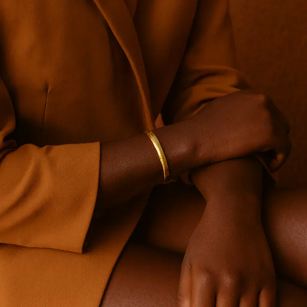 Close-up of a person wearing a gold bracelet on a brown background