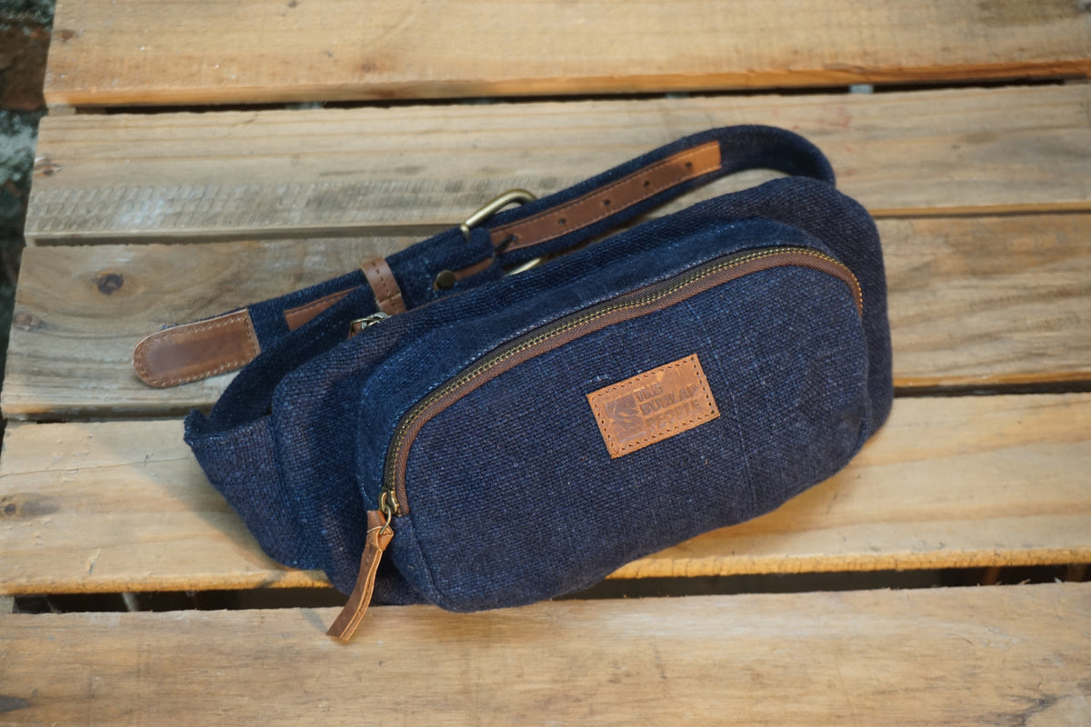 A navy blue canvas fanny pack with brown leather trim and a matching adjustable strap, resting on a rustic wooden plank surface.