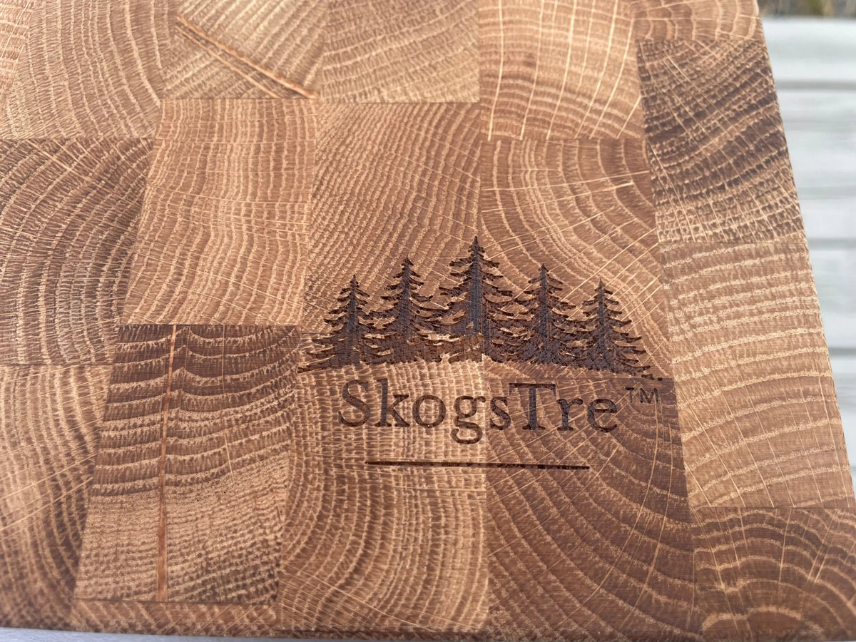 Close-up of a wooden cutting board with a block pattern and a dark engraved logo of five pine trees and the brand name 'SkogsTre' in the center.