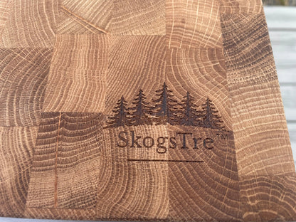 Close-up of a wooden cutting board with a block pattern and a dark engraved logo of five pine trees and the brand name 'SkogsTre' in the center.