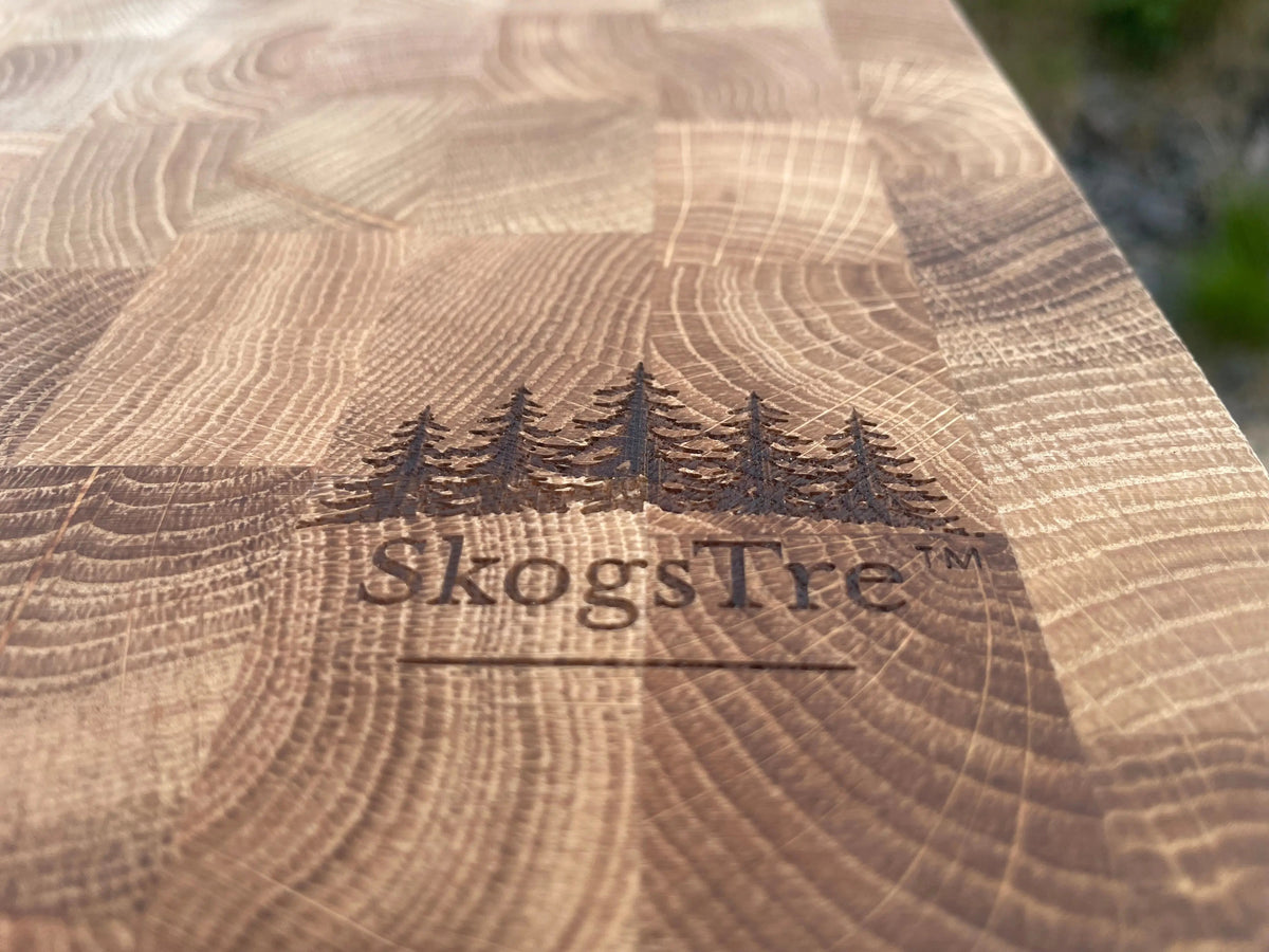 Close-up of a wooden cutting board with visible wood grain and the engraved brand name SkogsTre along with a forest tree logo.