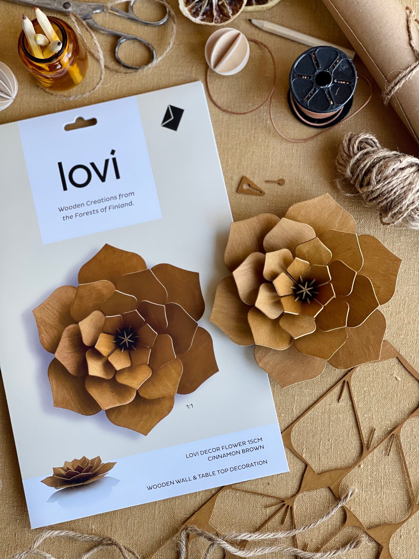 Wooden flowers with 'lovi' packaging on a craft table with supplies.
