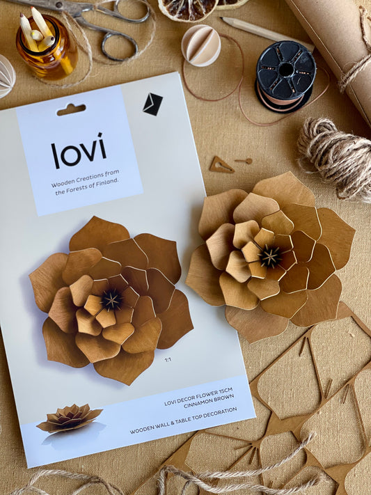 Wooden flowers with 'lovi' packaging on a craft table with supplies.