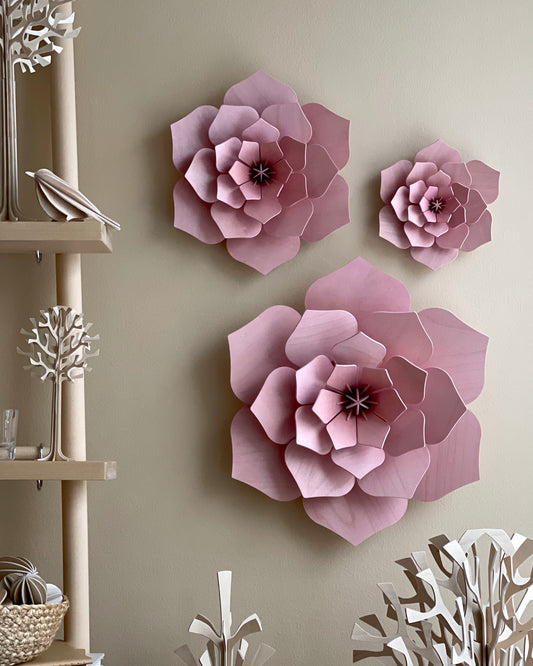 Three-dimensional pink paper flower wall decor pieces displayed on a beige wall in a styled interior setting.