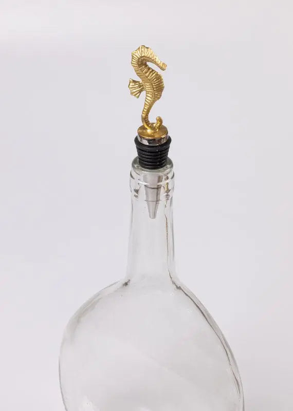 Clear glass bottle with a gold seahorse stopper on a white background