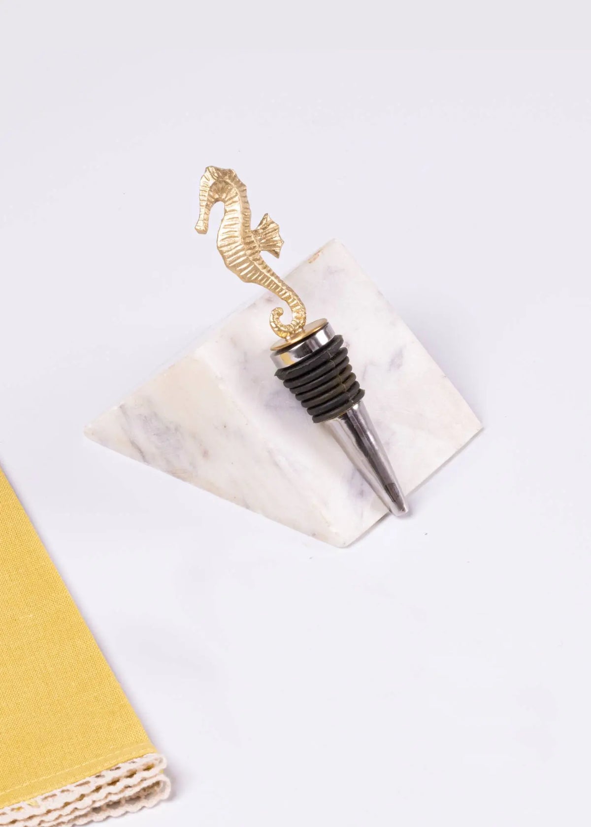Gold seahorse-shaped bottle stopper on a marble coaster with a white background