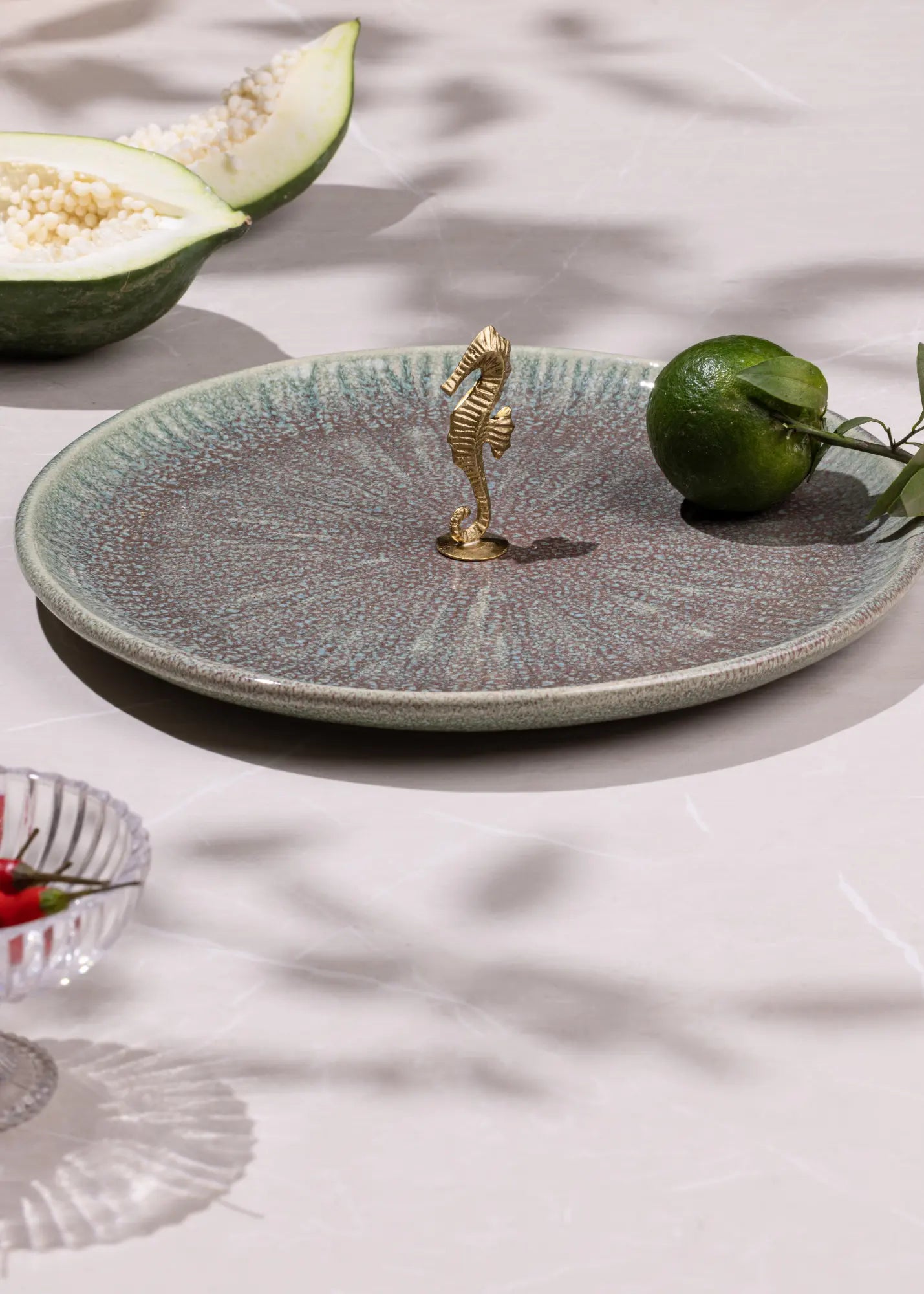 Decorative ceramic plate with a gold seahorse charm on a light surface with fruits.