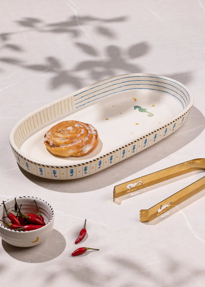 Rectangular ceramic tray with a pastry, small bowl of red peppers, and wooden tongs on a light surface.