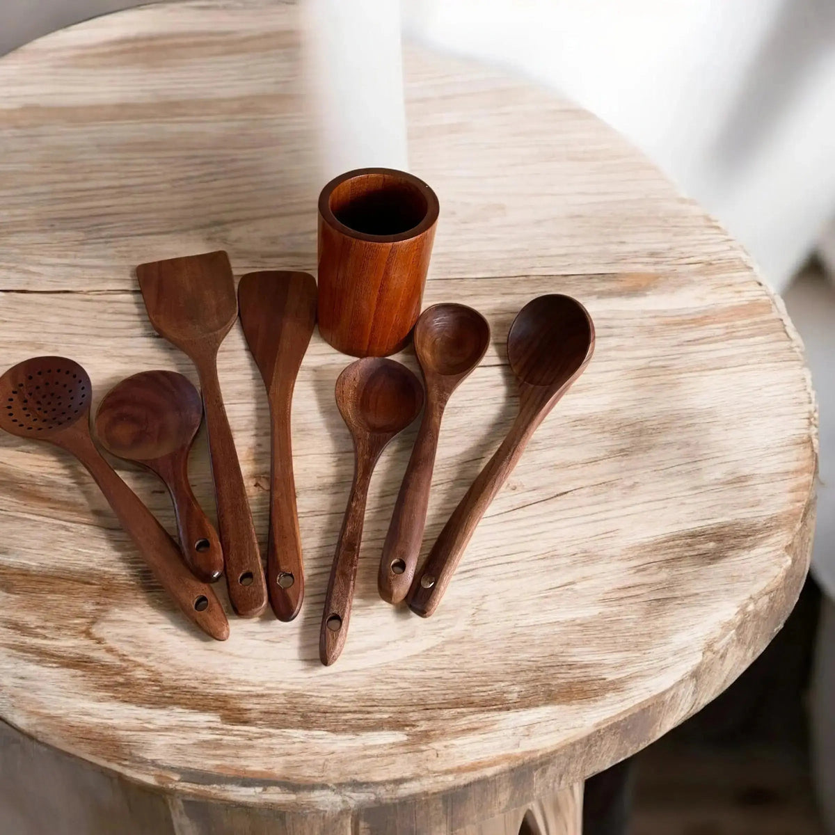 Set of wooden spoons and a small wooden cup on a round wooden table.