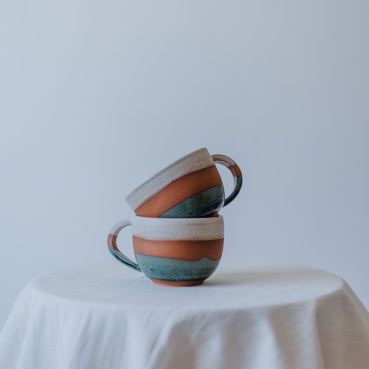 Stack of ceramic mugs with striped design on a white tablecloth against a light gray background