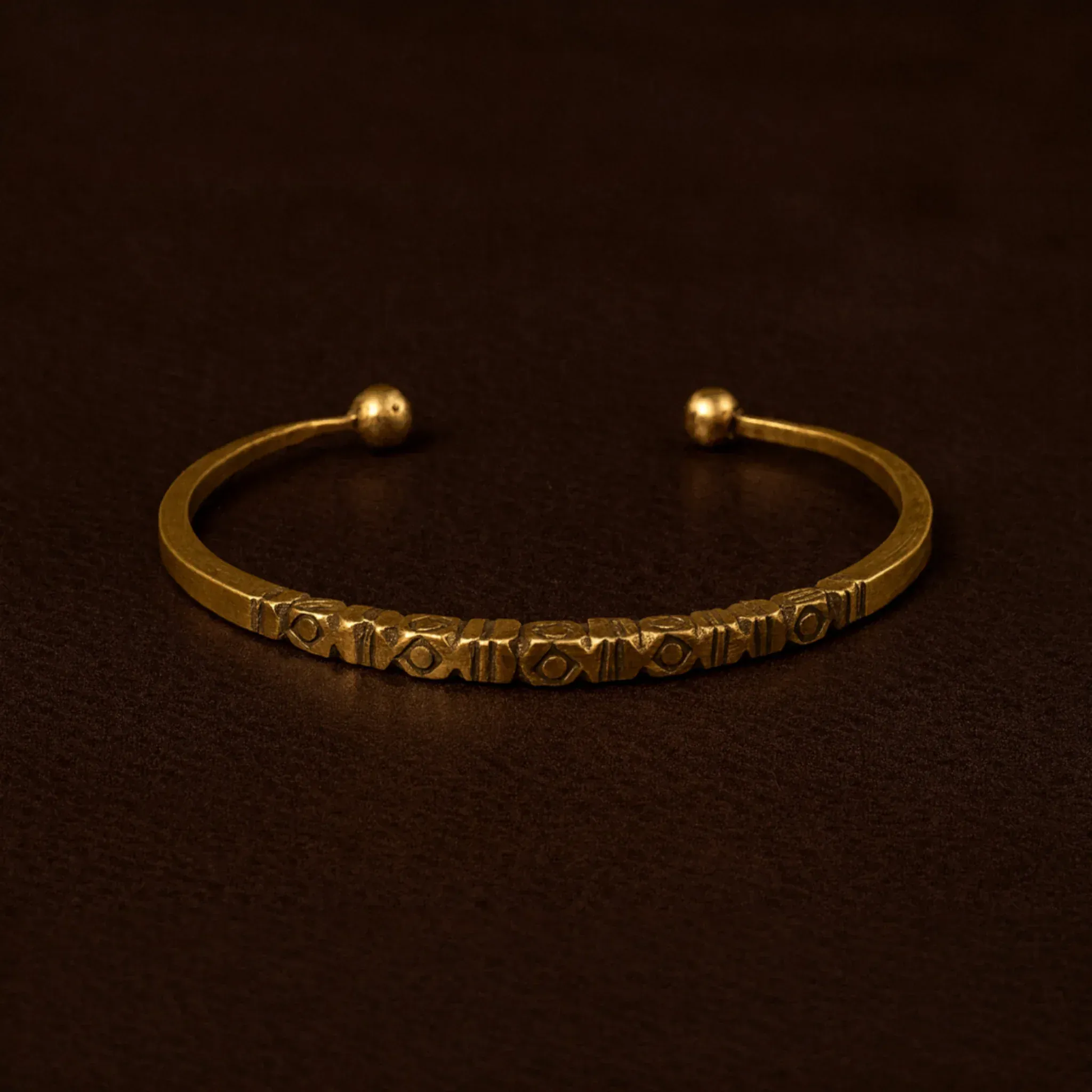 Gold bracelet with engraved details on a dark brown background