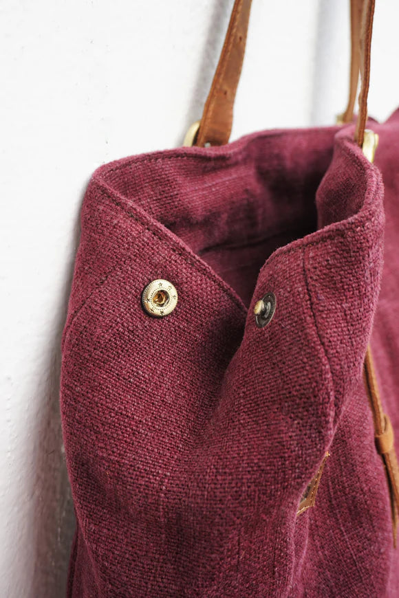 Close-up of a burgundy fabric bag with leather handles against a white background