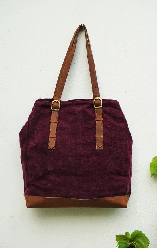 Maroon tote bag with brown handles and trim on a light background