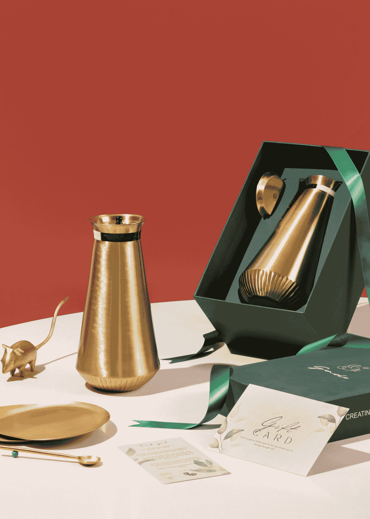 Gold brass carafe with packaging on a white surface against a red background