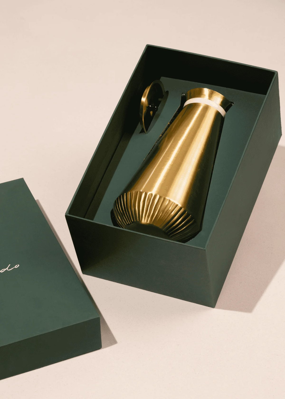 Gold metallic bottle in a green box on a beige background