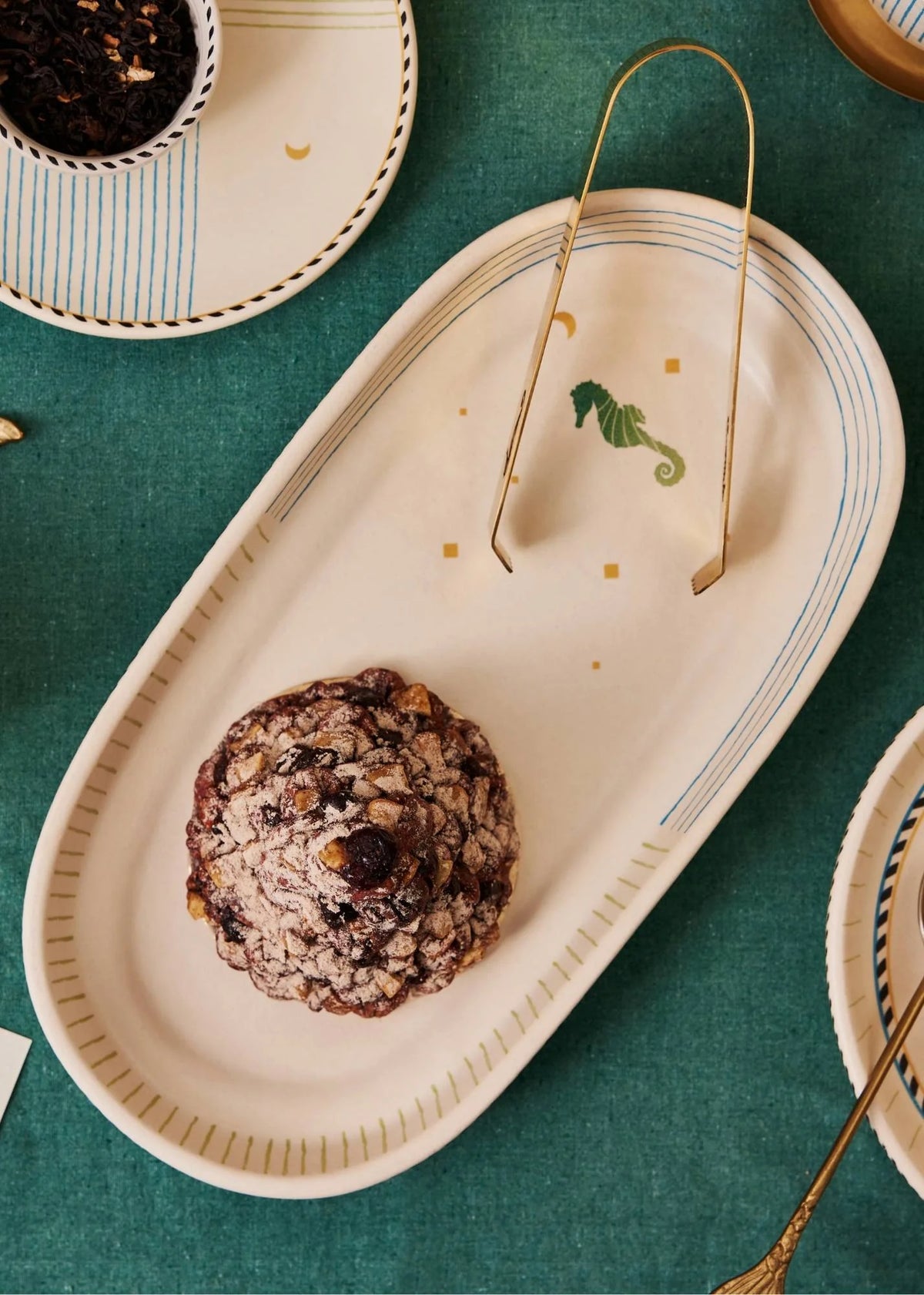 Oval ceramic plate with a decorative edge on a green tablecloth, featuring a cookie.
