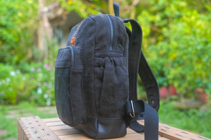 Black backpack on a wooden surface with a blurred green garden background