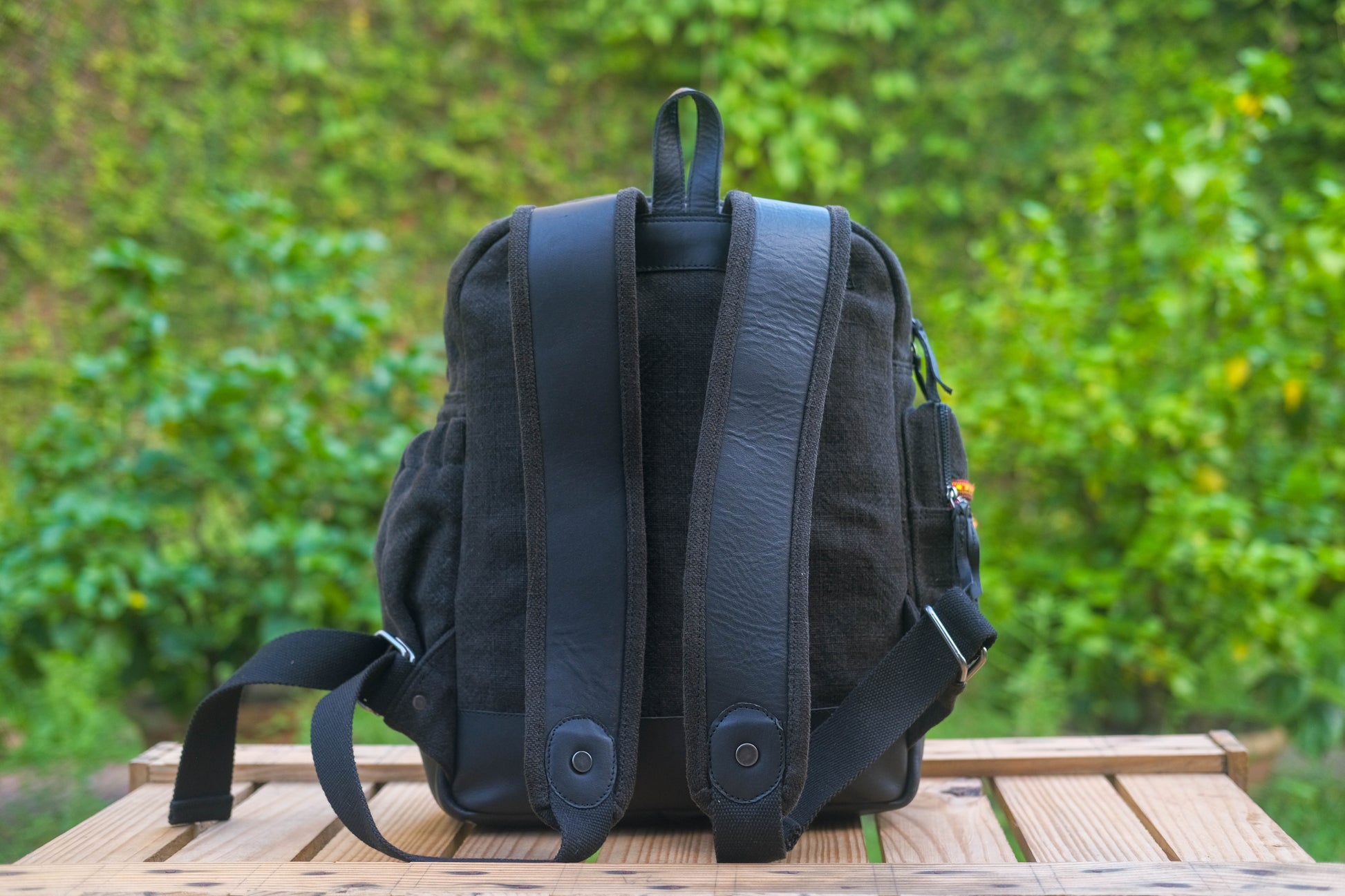 Black backpack on a wooden surface with a blurred green background