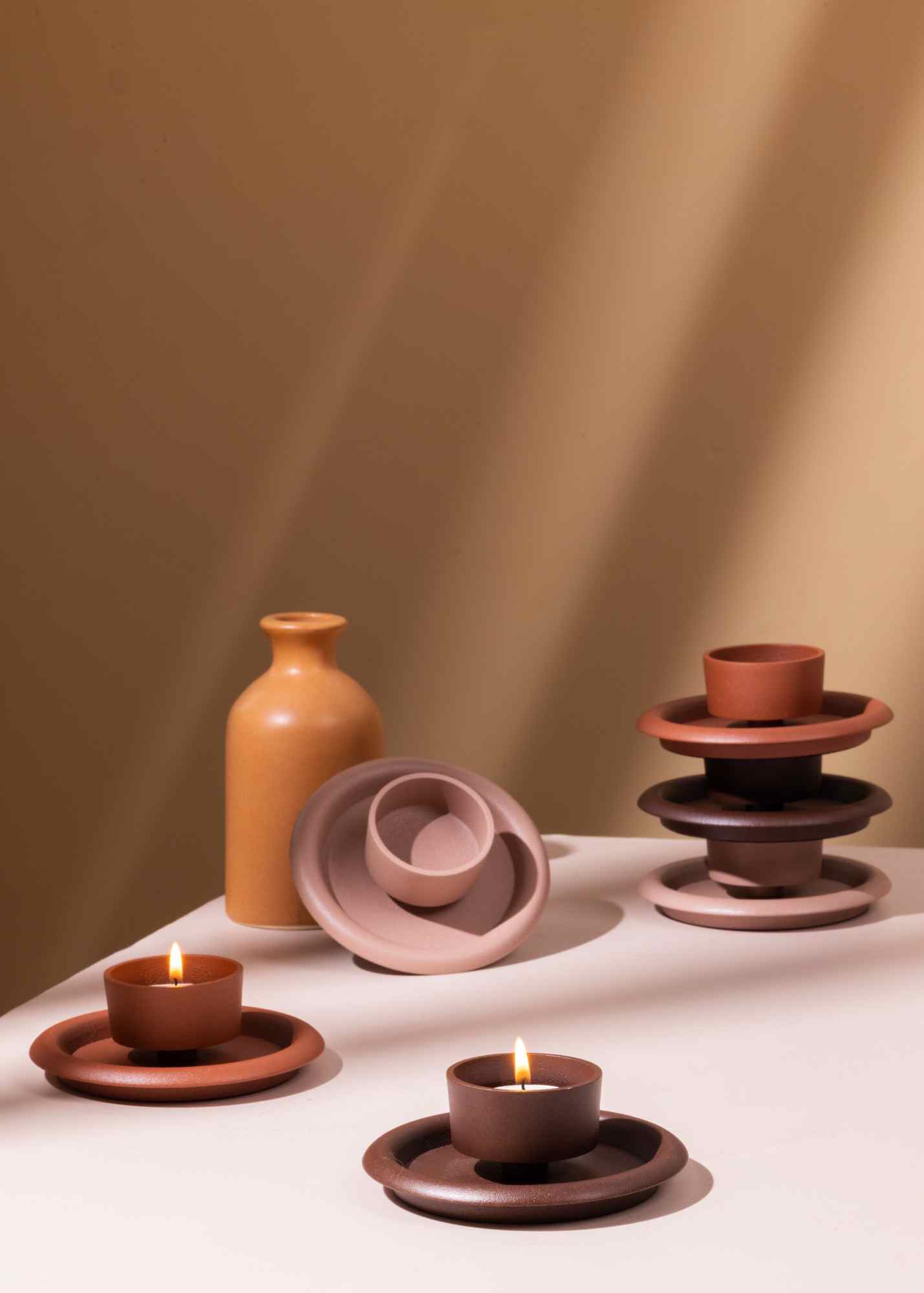 Set of ceramic items including vases, bowls, and candle holders on a white surface with a warm brown background.