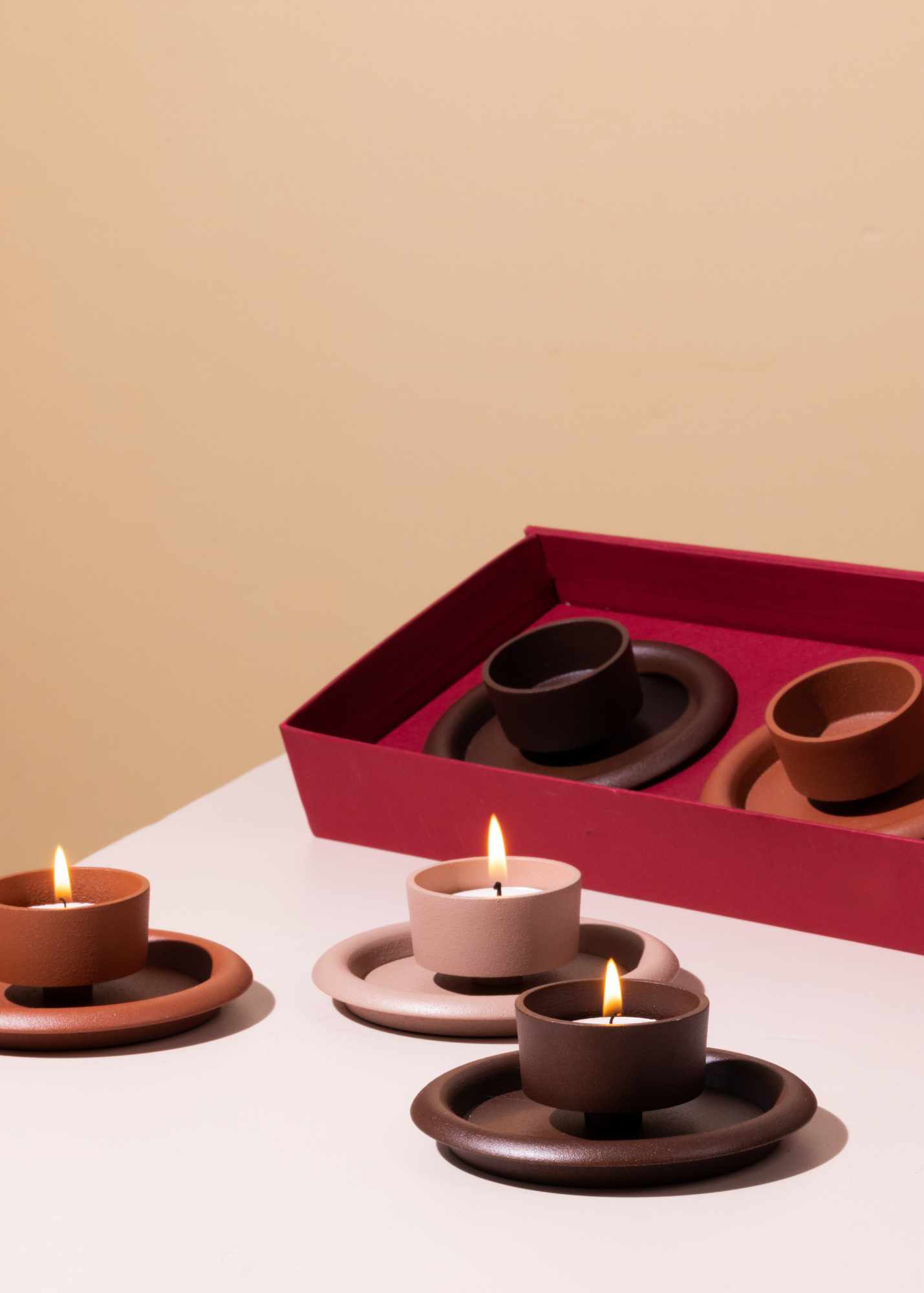 Set of ceramic candle holders with lit candles on a beige background