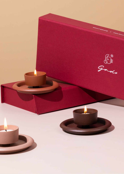 Ceramic candle holders with lit candles in front of a red box with 'godo' branding.